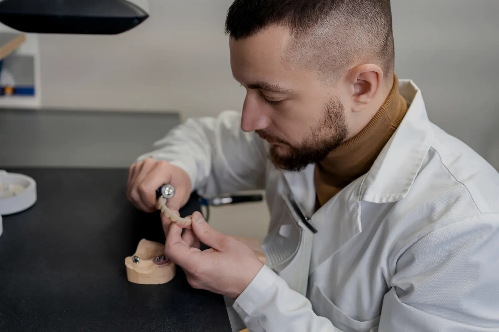 A dental technician working on a restoration at a laboratory bench